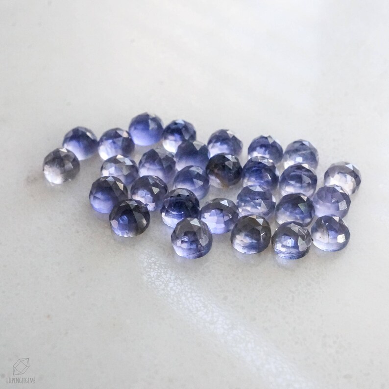 May include: A collection of 20 faceted, purple-blue gemstone beads. The beads are round and have a smooth, polished finish.