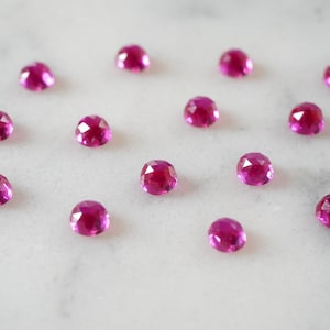Może przedstawiać: Kolekcja 14 fasetowanych różowych kamieni szlachetnych na białym marmurowym tle.
