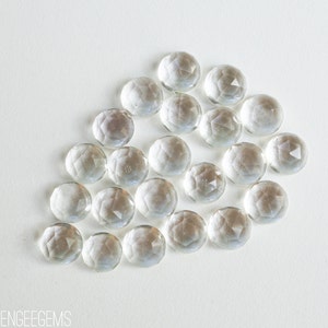 May include: A group of clear glass gems with a faceted design. The gems are arranged in a loose, organic pattern on a white background.