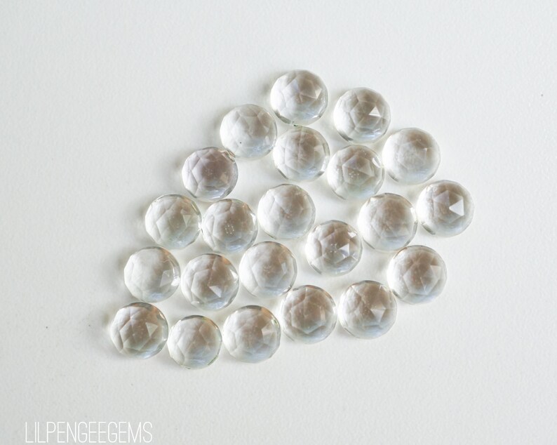 May include: A group of clear glass gems with a faceted design. The gems are arranged in a loose, organic pattern on a white background.