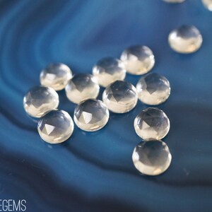 May include: A group of clear, faceted gemstones on a blue background. The gemstones are round and have a smooth, polished finish.