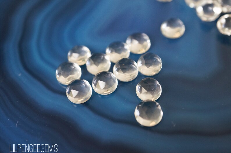 May include: A group of clear, faceted gemstones on a blue background. The gemstones are round and have a smooth, polished finish.