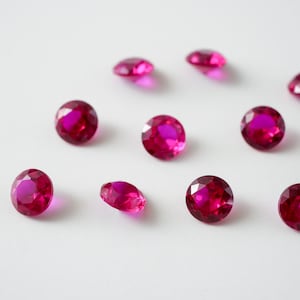 May include: Ten round, faceted, pink gemstones on a white background.