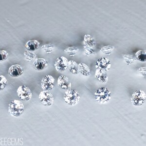 May include: A collection of clear, round, faceted gemstones, scattered on a white surface.