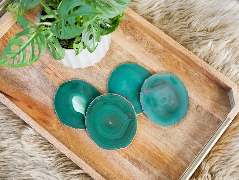 May include: Four green agate coasters on a wooden tray. The coasters are round and have a natural, organic look.