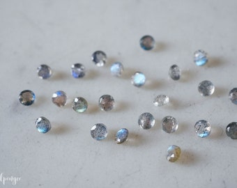 May include: A collection of round, iridescent labradorite gemstones in various shades of blue and grey. The stones are scattered on a white surface.