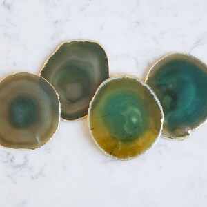 May include: Four agate coasters with gold trim. The coasters are green, yellow, and brown with a swirling pattern.