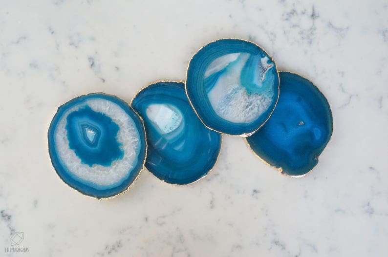 May include: Four blue agate coasters with gold trim. The coasters are round and have a natural, organic shape. They are perfect for protecting surfaces from scratches and spills.