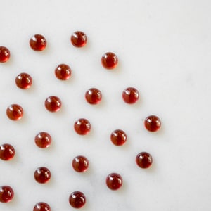 May include: A white surface with a scattered arrangement of small, round, red glass gems.