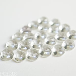 May include: A group of clear, faceted, round gemstones arranged in a loose circle on a white background.