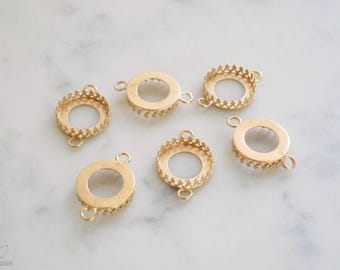 Könnte beinhalten: Eine Sammlung goldfarbener Lünettenfassungen für die Schmuckherstellung. Die Fassungen sind rund mit dekorativen Rändern und kleinen Schlaufen zum Befestigen. Sie sind auf einer weißen Marmoroberfläche angeordnet.