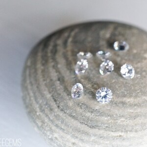 May include: A close-up of eight clear round gemstones on a gray stone. The gemstones are arranged in a random pattern.