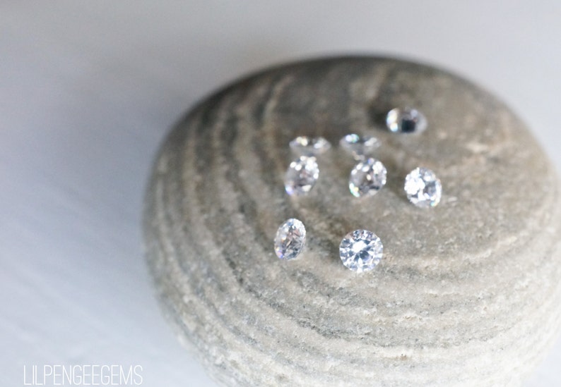 May include: A close-up of eight clear round gemstones on a gray stone. The gemstones are arranged in a random pattern.