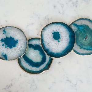 May include: Four teal and white agate coasters with gold trim. The coasters are round and have a natural, organic look.