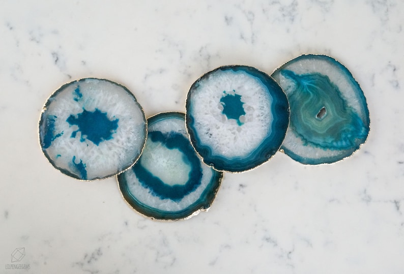 May include: Four teal and white agate coasters with gold trim. The coasters are round and have a natural, organic look.