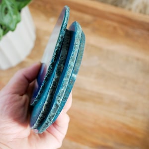 May include: Three blue agate coasters stacked on top of each other. The coasters have a natural, rough edge and a smooth, polished surface.