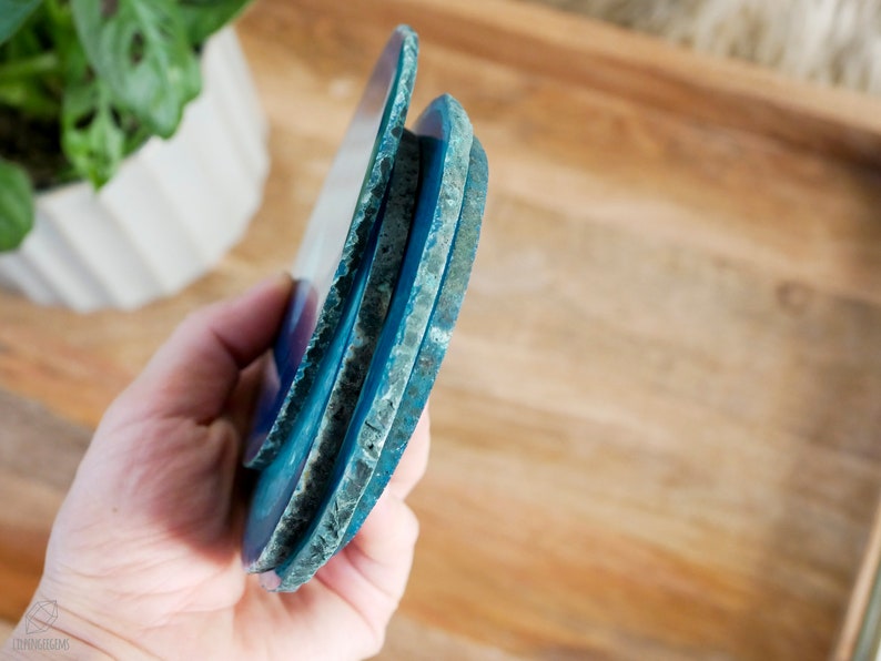 May include: Three blue agate coasters stacked on top of each other. The coasters have a natural, rough edge and a smooth, polished surface.