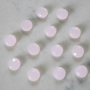 Puede incluir: Una colección de 13 gemas redondas y facetadas de color rosa pálido dispuestas en círculo sobre una superficie de mármol blanco.