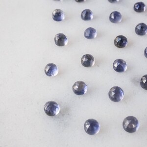 May include: A collection of 20 faceted, round, blue gemstones on a white surface.
