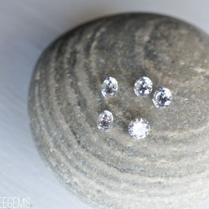 May include: Five clear round gemstones on a gray textured rock.