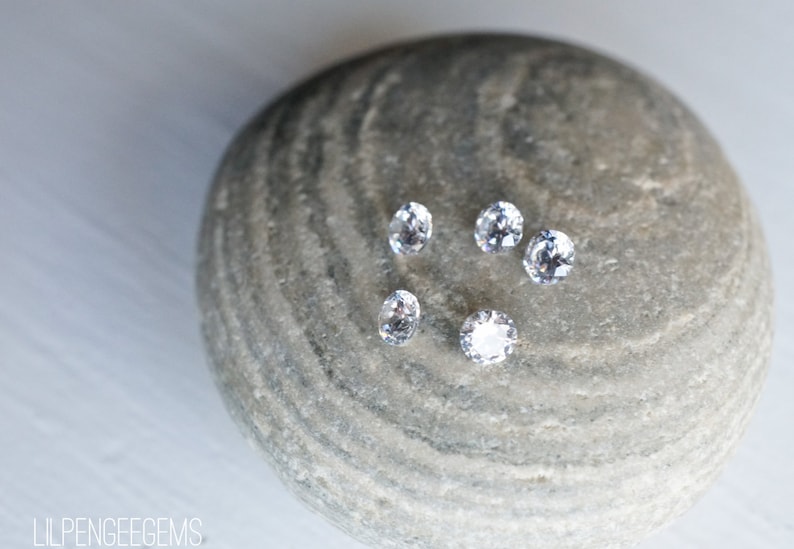 May include: Five clear round gemstones on a gray textured rock.