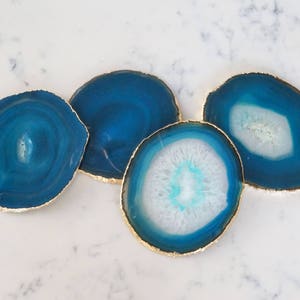 May include: Four blue agate coasters with gold trim. The coasters are round and have a natural, organic shape. They are perfect for protecting surfaces from scratches and spills.