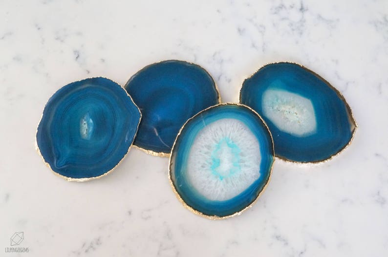 May include: Four blue agate coasters with gold trim. The coasters are round and have a natural, organic shape. They are perfect for protecting surfaces from scratches and spills.
