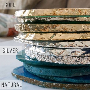 May include: Stack of agate coasters in natural, silver, and gold finishes. The coasters are round and have a rough, natural edge.