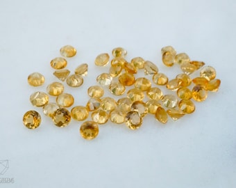 May include: A group of 30 round, faceted, yellow citrine gemstones. The stones are loose and scattered on a white surface.