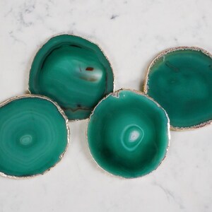 May include: Four green agate coasters with gold trim. The coasters are round and have a natural, organic look.