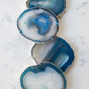 May include: Four blue agate coasters with silver trim. The coasters are round and have a natural, organic look. They are perfect for adding a touch of elegance to any home.