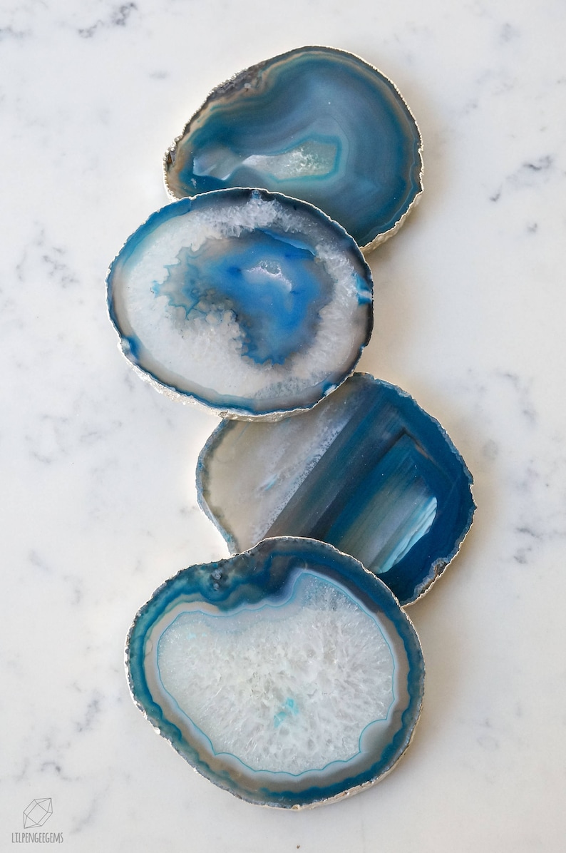 May include: Four blue agate coasters with silver trim. The coasters are round and have a natural, organic look. They are perfect for adding a touch of elegance to any home.