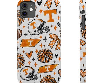 Può includere: Una cover per smartphone bianca con un motivo ripetuto di caschi da football americano arancioni e bianchi con logo T, fiocchi a scacchi arancioni e bianchi, pon pon arancioni, contorni dello stato del Tennessee arancioni con una T, cuori e stelle.