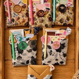 Puede incluir: Cinco sobres de papel rectangulares con estampados florales, cada uno sellado con lacre y que contiene tarjetas de rese&ntilde;as de libros, pegatinas y un bol&iacute;grafo. Los sobres muestran varios dise&ntilde;os con flores silvestres y rosas.