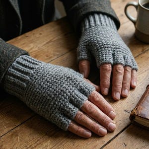 May include: A pair of grey fingerless gloves featuring a textured knit pattern and a ribbed cuff. The gloves cover the palm and the back of the hand while leaving the fingers exposed, providing a snug fit around the wrist and hand area.