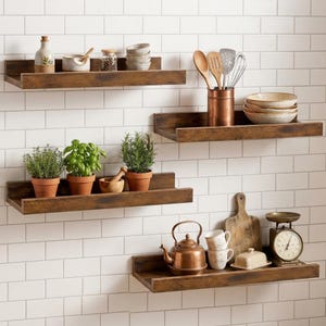 Puede incluir: Cuatro estantes flotantes de madera marrón oscuro montados en una pared de azulejos blancos. Los estantes contienen varios artículos de cocina, incluyendo hierbas en macetas, cuencos de cerámica, una tetera de cobre y una báscula de cocina.