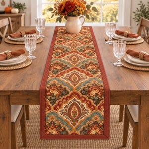 May include: A long rectangular table runner featuring a repeating damask pattern in shades of rust orange, teal, and cream. The runner has a solid rust-colored quilted border and is centered on a wooden dining table with place settings.