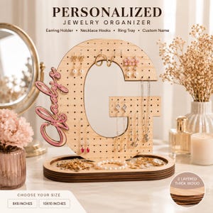 May include: A light-colored wooden jewelry organizer shaped like the letter G, featuring a perforated surface for earrings, necklace hooks, and a ring tray base. The name Gladys is attached in pink script. Text includes Personalized Jewelry Organizer.