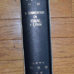 May include: A black hardcover book spine with gold lettering titled A Commentary on Psalms by Y.S. Park, featuring Korean text including the title and author name, encased in a light-colored protective slipcase with thin gold horizontal lines.