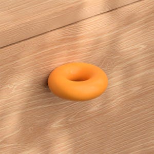 Könnte beinhalten: Ein glatter, massiver orangefarbener Möbelknopf in Form eines Torus oder Donuts. Der Knopf ist auf einer hellen Holzoberfläche mit sichtbarer Maserung montiert und weist eine abgerundete, durchgehende Kreisform mit einer Öffnung auf.