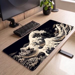 May include: A rectangular desk mat featuring a high-contrast graphic print of stylised ocean waves in cream and gold tones against a deep black background. The design covers the entire surface of the mat, which is positioned on a wooden desk.