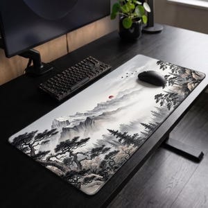 Può includere: Un tappetino da scrivania rettangolare con un'illustrazione paesaggistica a inchiostro bianco e nero raffigurante montagne frastagliate, pini e un piccolo sole rosso. Il tappetino è posizionato su una superficie scura con tastiera e mouse.