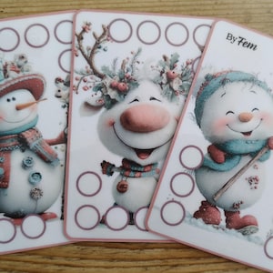 Op de afbeelding: Drie rechthoekige kaarten met illustraties van een sneeuwpop met hoge hoed, een rendier met bloemen in het gewei en een sneeuwpop met een grote lolly. Elke kaart heeft een witte achtergrond, roze randen en lege cirkels.