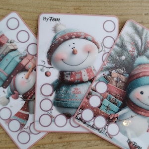 Op de afbeelding: Drie rechthoekige witte kaarten met illustraties van sneeuwpoppen met mutsen en sjaals, vergezeld van stapels kleurrijke geschenkdozen. Elke kaart bevat de tekst By Fem en een reeks lege cirkels voor het bijhouden van voortgang.