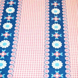 Op de afbeelding: Een stof met een herhalend patroon van verticale donkerblauwe strepen afgewisseld met lichtroze en witte gingham-secties. De blauwe strepen zijn versierd met een herhalend bloemmotief in de kleuren wit, lichtblauw en roze.