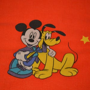 May include: A bright orange fabric featuring a graphic print of Mickey Mouse and Pluto standing together. Mickey Mouse is wearing a purple jacket and blue shoes, while Pluto is yellow with black ears. A small yellow star is printed to the right.