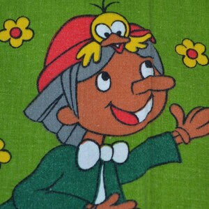 Può includere: Un tessuto verde con una stampa a cartoni animati ripetuta di un personaggio con capelli grigi, un cappello rosso e un uccellino giallo sulla testa. Il personaggio indossa una giacca verde scuro con colletto bianco ed è circondato da fiori.