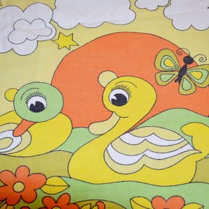 Può includere: Un tessuto giallo con una stampa raffigurante due anatre, una con la testa verde e una con la testa gialla, davanti a un grande sole arancione. Il disegno include nuvole bianche, stelle gialle, una farfalla verde e fiori arancioni.