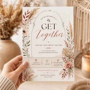 May include: A rectangular invitation card featuring an arched frame decorated with dried pampas grass, flowers, and foliage in shades of rust, beige, and green. The text reads: You're invited to a Get Together, Good Food, Great Company, Good Times.