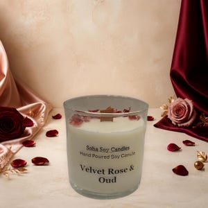 May include: A clear glass candle jar filled with white soy wax and a wooden wick. The label reads Soha Soy Candles Hand Poured Soy Candle Velvet Rose & Oud. Dried rose petals are scattered on the surface of the wax inside the glass container.